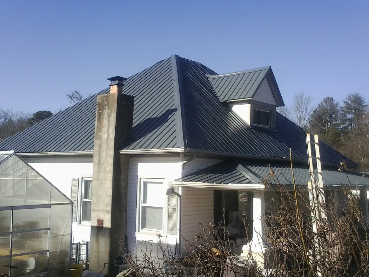 Dark blue standing seam metal roof on a white farmhouse with dormer — Slate & Tile Roof Repair by Roofing Brothers in Union Springs