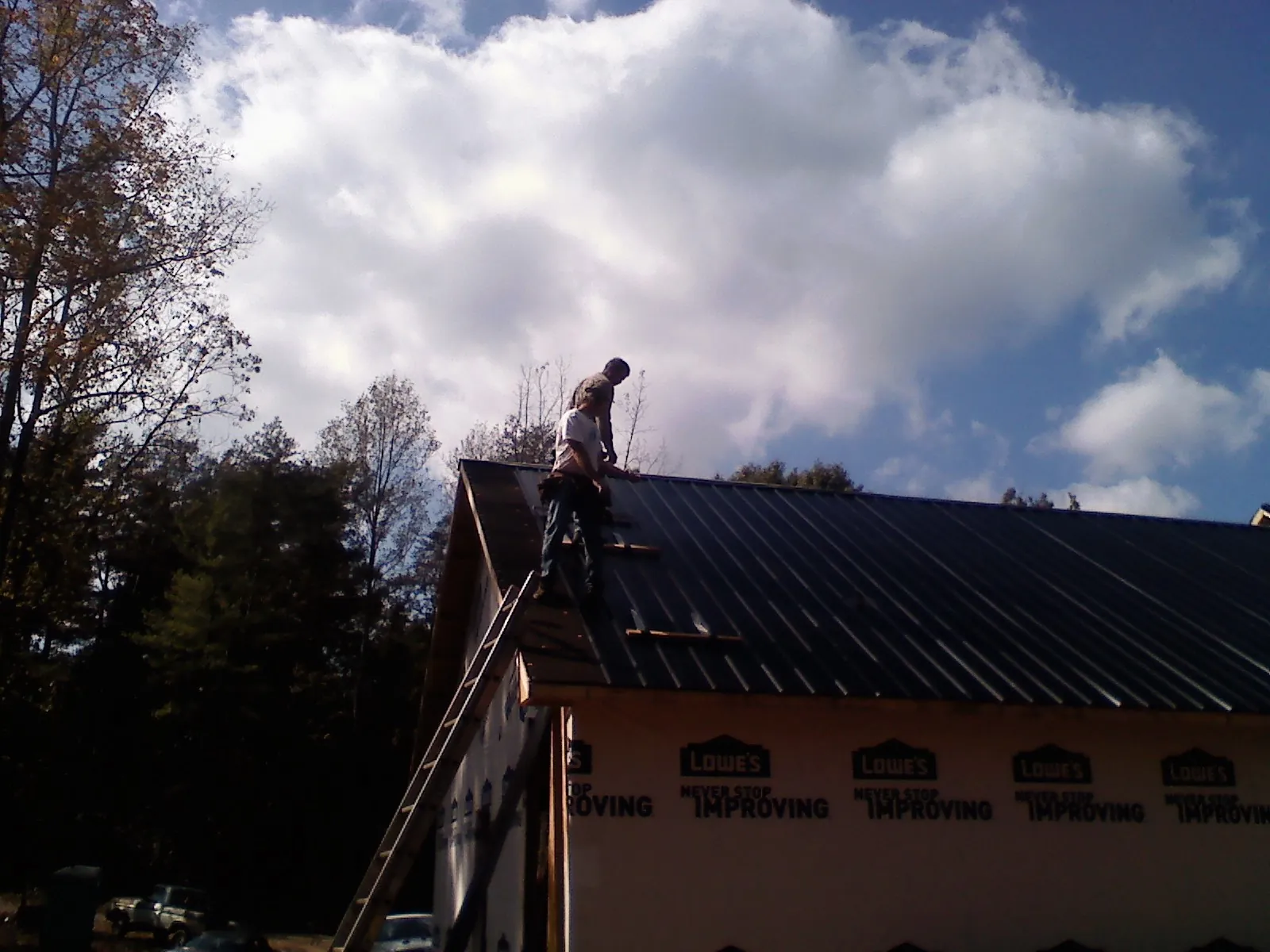 Roofer fastening dark metal panels high against a cloudy sky, from a Roof Inspection job in Union Springs